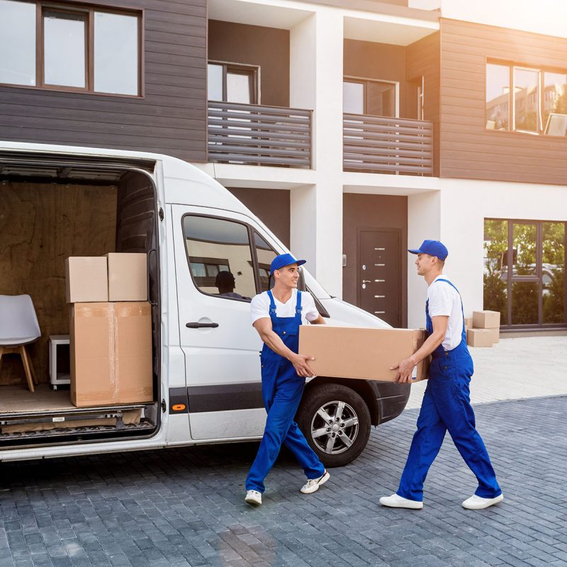 Two removal company workers are loading boxes into a minibus.